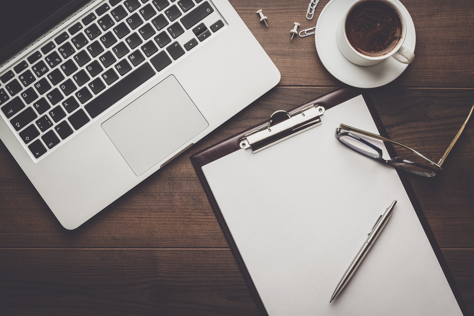 top view of an office table. brown wooden office desk with cup of coffee, notepad and laptop computer. working office space. office objects on the table. office working atmosphere