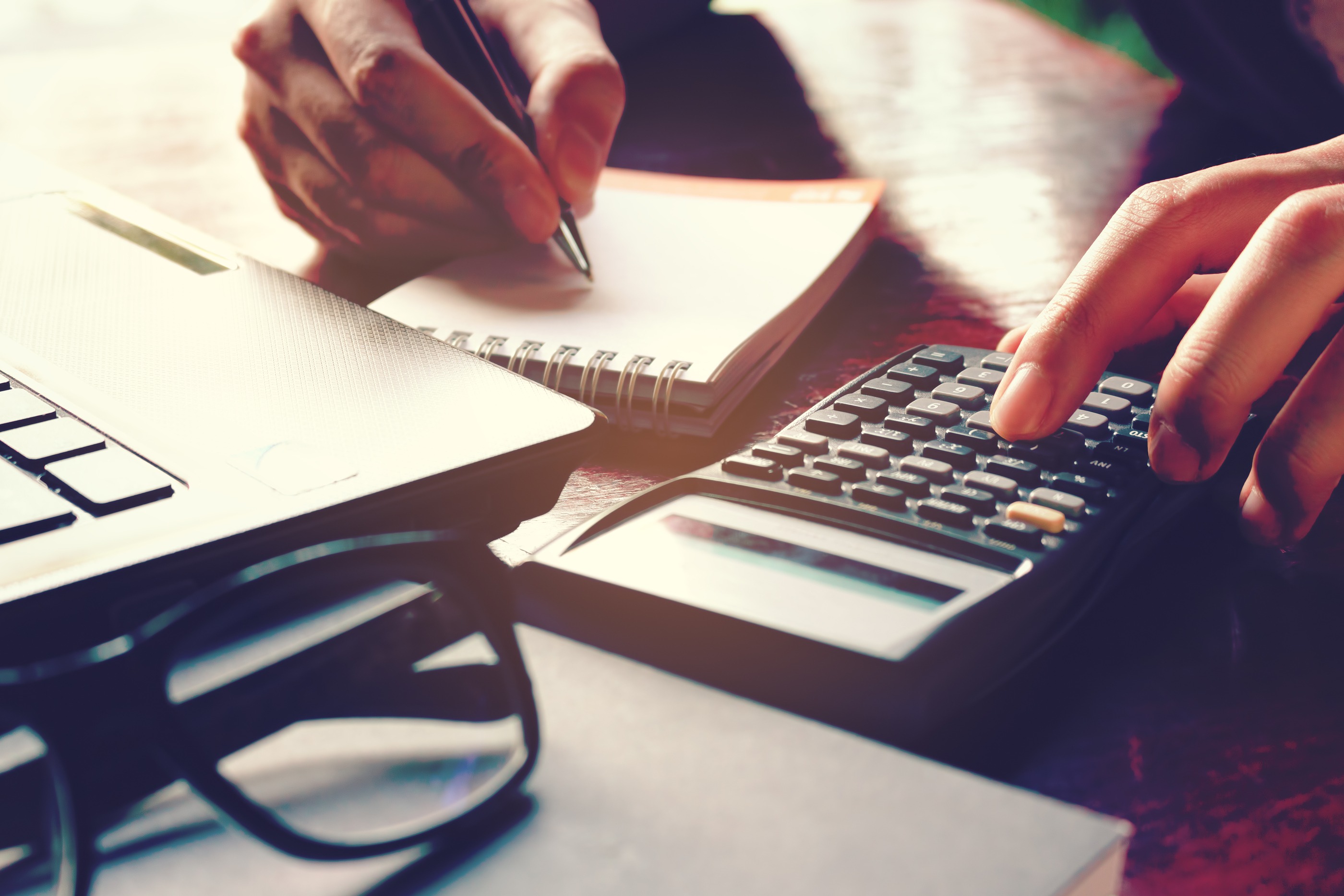 Close up woman hand using calculator and writing make note with calculate about cost at home office.